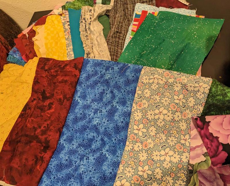 colored rectangles of cotton quilting fabric sewn together on the long edge to make a larger strip of fabric, sitting on top of a pile of unsewn fabric rectangles