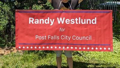 Randy standing in a lawn holding a large banner that says Randy Westlund for Post Falls City Council