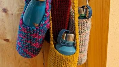 four crochetted water bottle carriers with water bottles in them