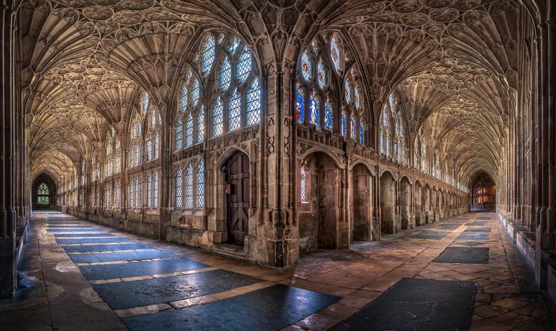 the cloisters at gloucester cathedral: the intersection of two long stone hallways lined with windows, stained glass, and elaborate archways
